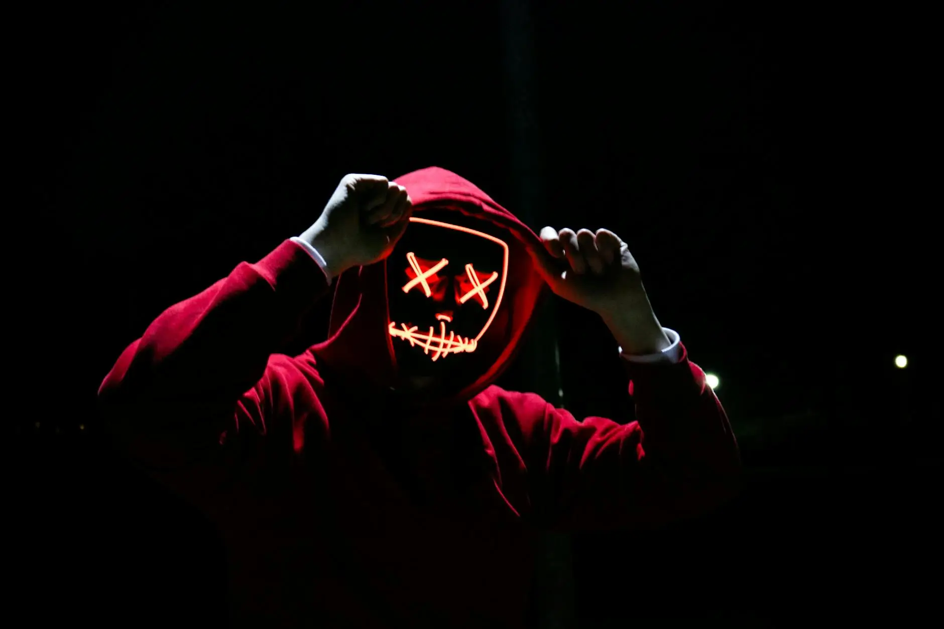 A spooky illuminated mask figure with a red hoodie in a dark setting, perfect for Halloween themes.